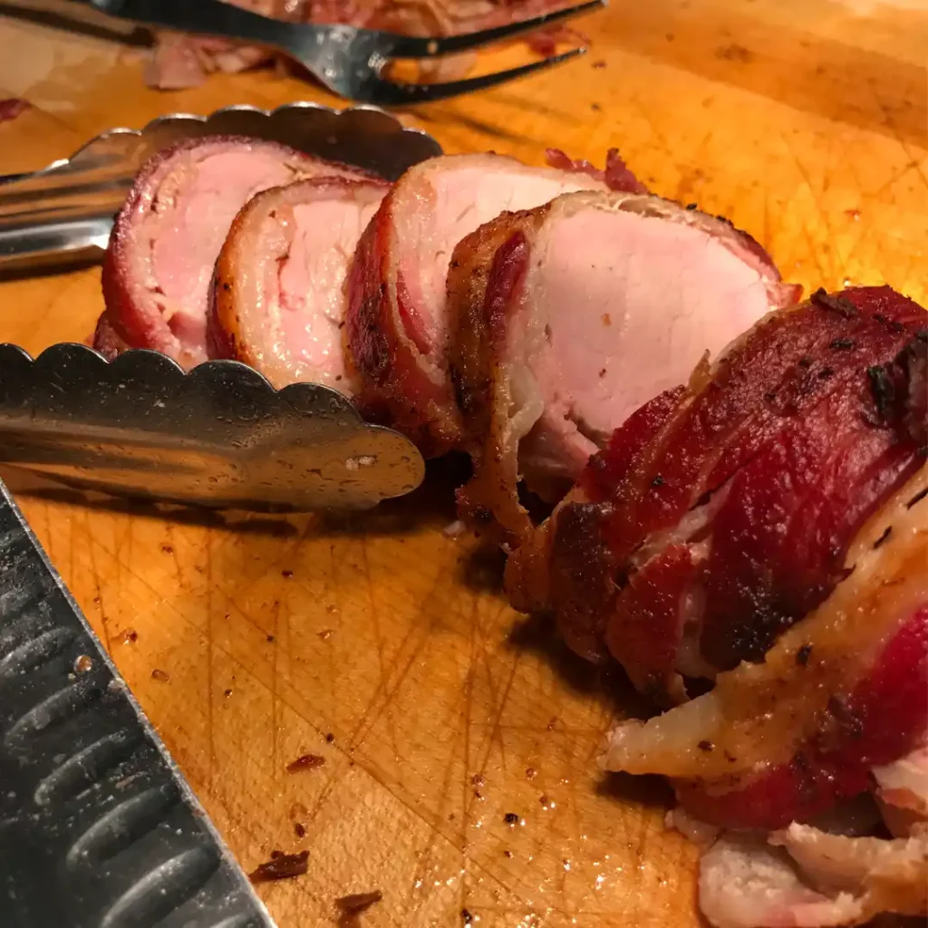 Carved Bacon Wrapped Pork Tenderloin displayed on a cutting board